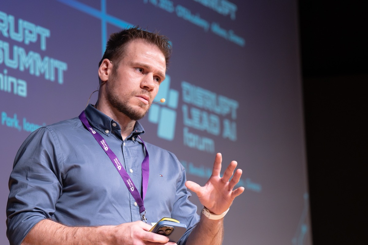 Ioannis Papikas speaking on stage at Disrupt AI Summit, mid-sentence with one hand raised